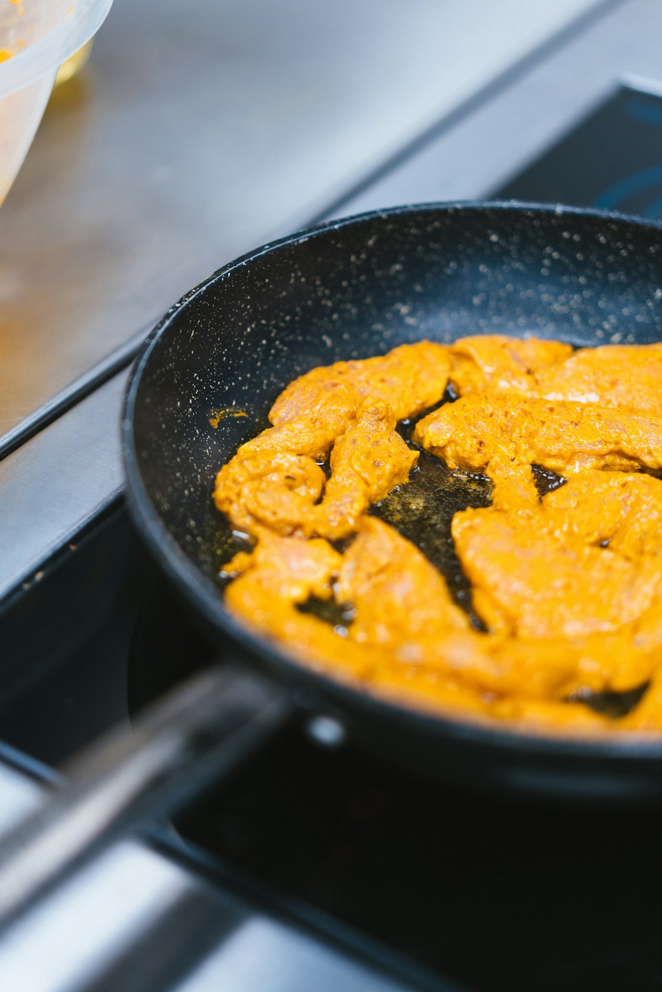 Marinated chicken pieces frying in a pan on the stove.