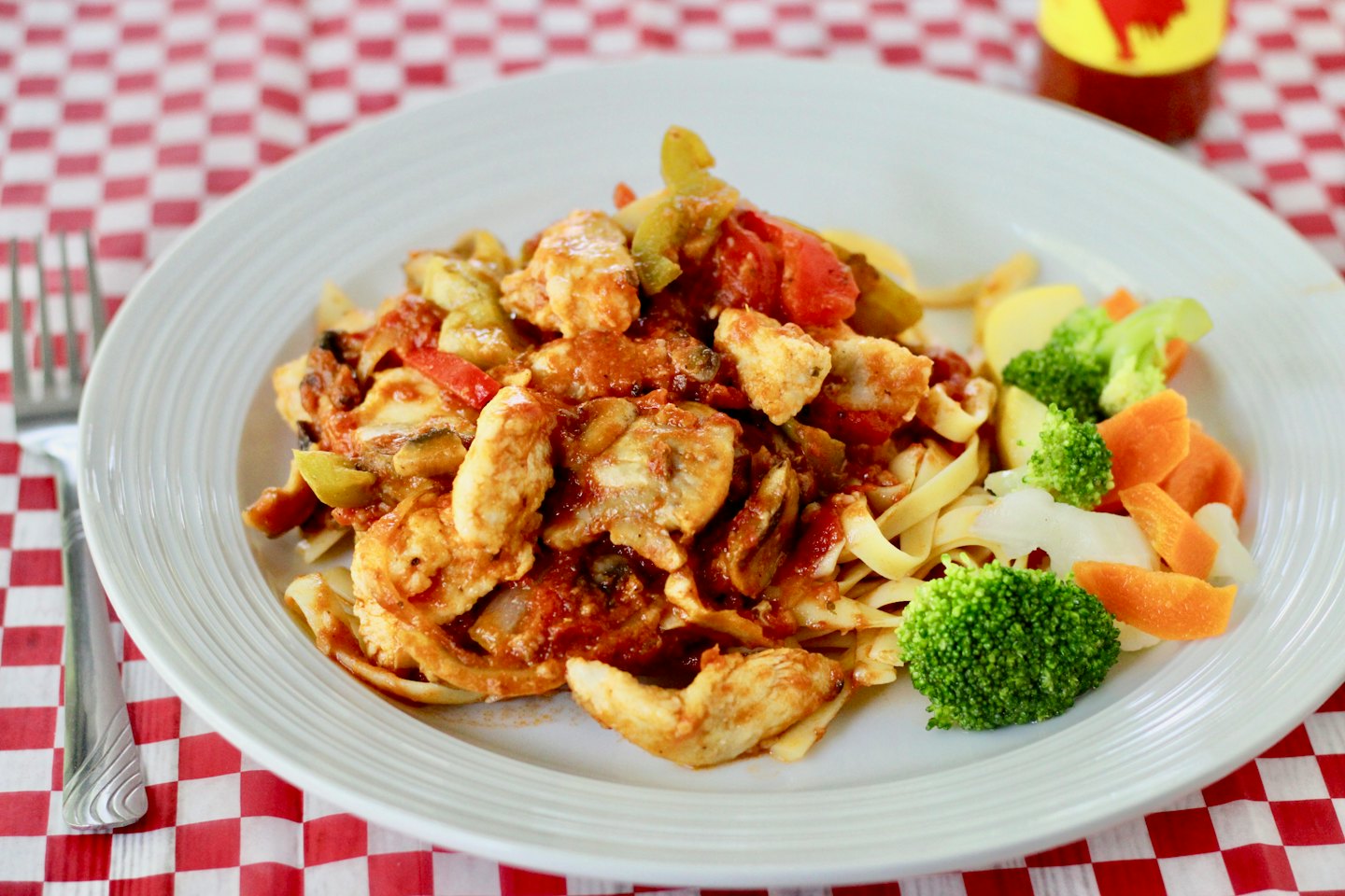 Chicken and vegetable pasta on a checkered tablecloth.
