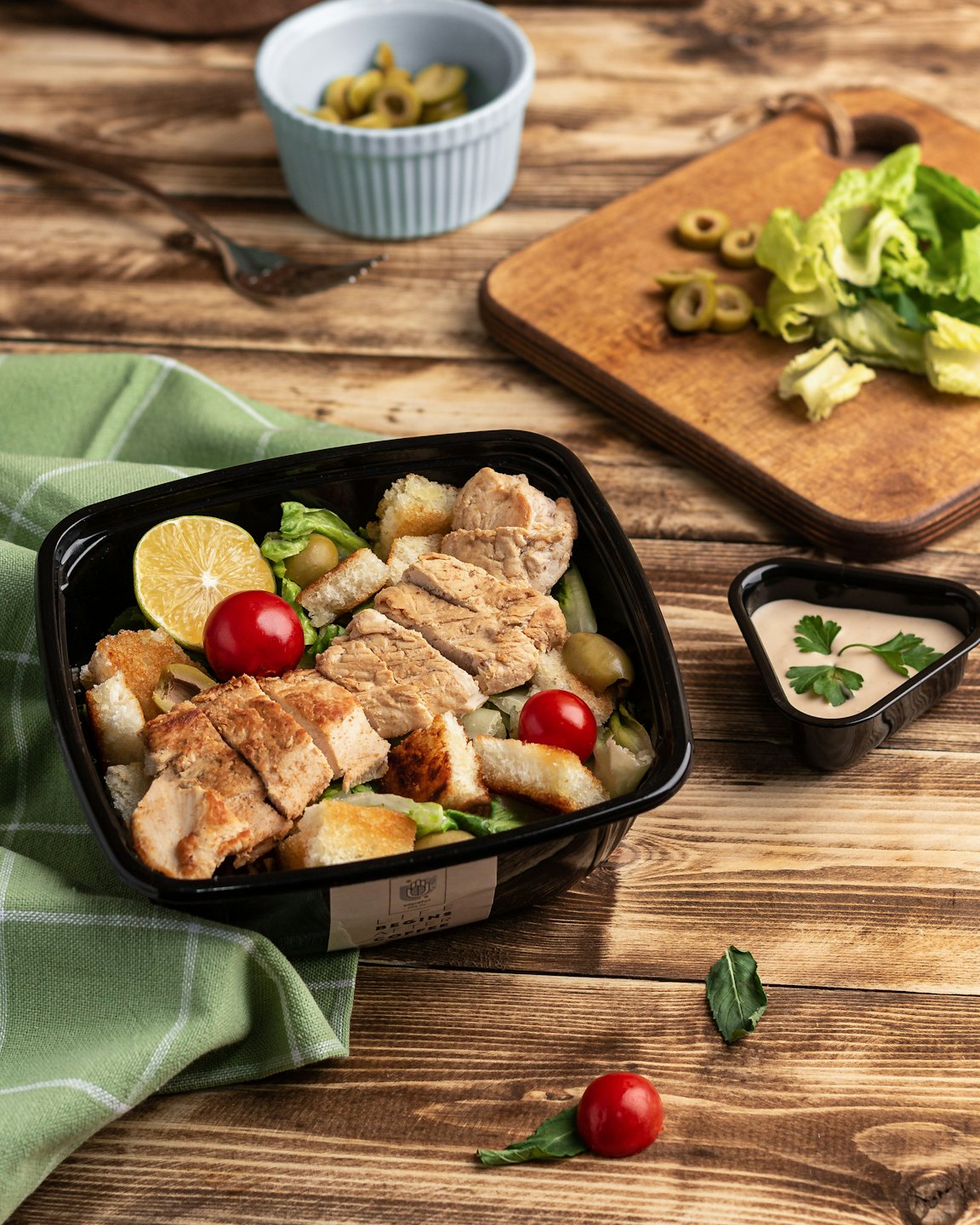 Chicken Caesar salad in a black takeout container on a wooden table.