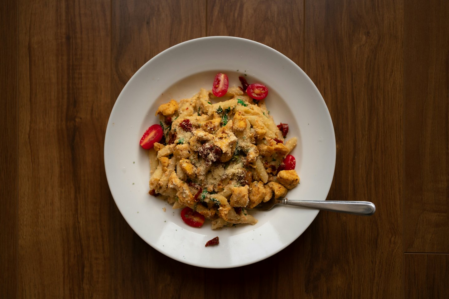 Penne pasta with chicken and vegetables on a wooden table.