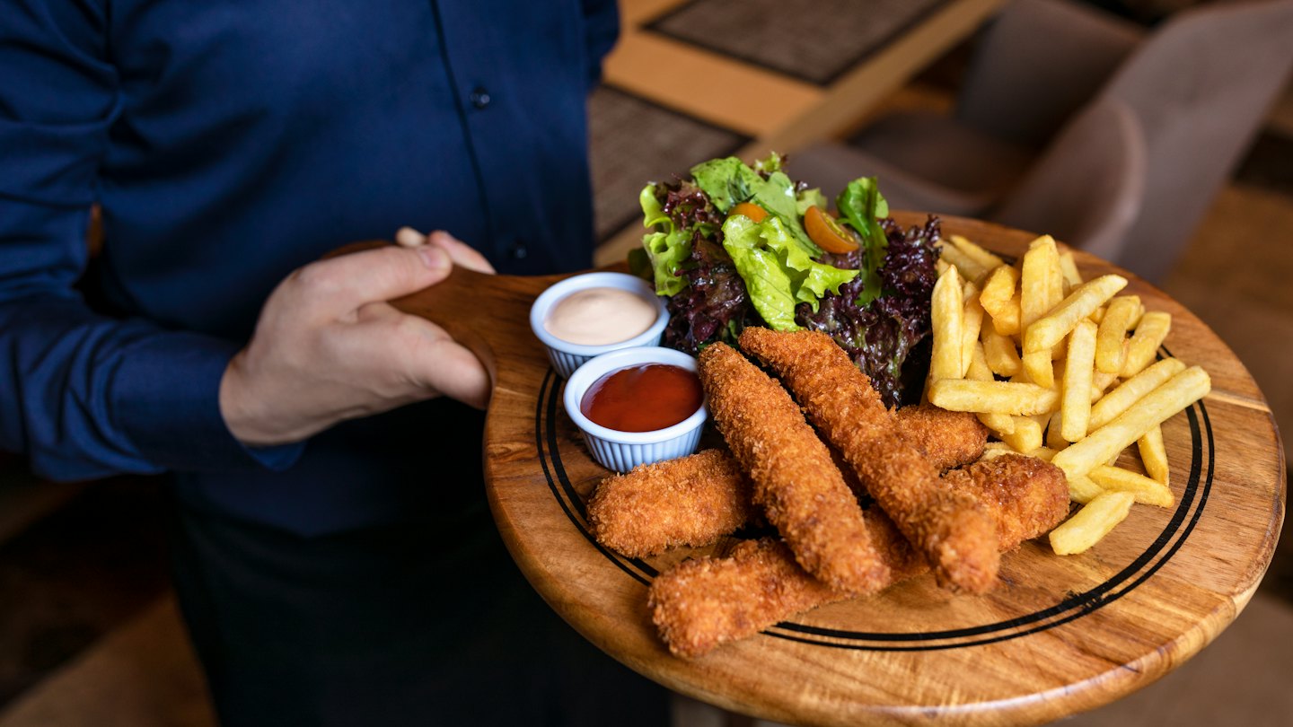 Server presents a platter of chicken tenders, fries, and salad.