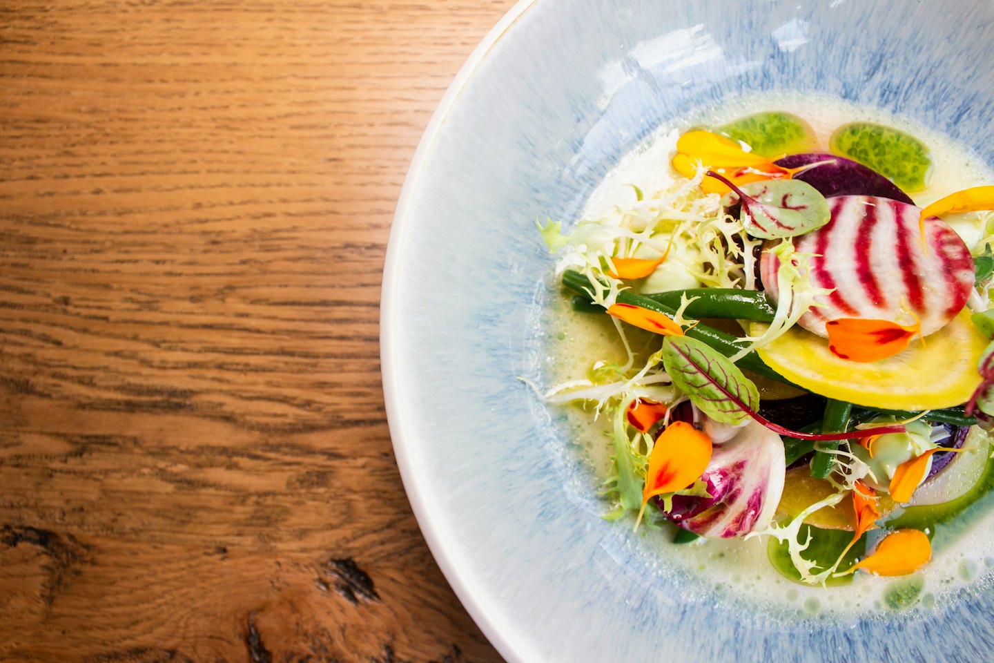 Fresh salad with vegetables and edible flowers in a blue bowl.